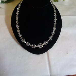 May include: A clear crystal necklace with round beads on a black velvet background.