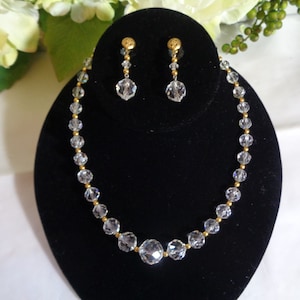 Peut inclure: Un collier et des boucles d'oreilles en cristal avec des accents dorés. Le collier est composé de perles de cristal claires et les boucles d'oreilles sont de style pendantes avec une seule perle de cristal.
