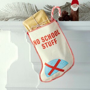 Pode incluir: Uma meia de Natal branca com detalhes vermelhos e o texto "NO SCHOOL STUFF" em letras vermelhas. Um X vermelho é desenhado sobre um transferidor azul na meia.
