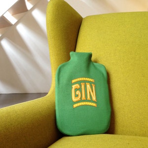 May include: A green fabric hot water bottle with the word "GIN" in yellow letters on a yellow armchair.