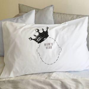 Könnte beinhalten: Weißer Kissenbezug mit einer schwarzen Krone und dem aufgedruckten Text "Mum's Head". Die Krone befindet sich über einem gestrichelten Umriss eines Kopfes.