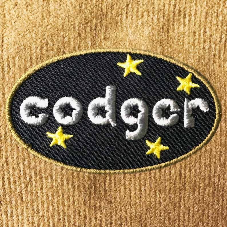 Op de afbeelding: Zwarte ovale patch met witte geborduurde tekst "codger" en gele steraccenten.
