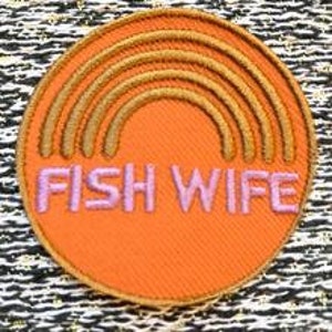 May include: Orange round embroidered patch with a gold rainbow and the text "FISH WIFE" in pink.
