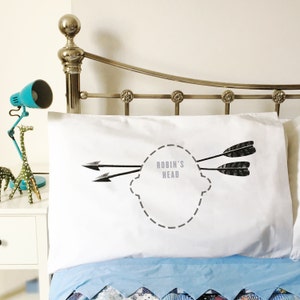 Könnte beinhalten: Weißer Kissenbezug mit einer schwarz-weißen Grafik von zwei Pfeilen, die auf einen gestrichelten Umriss eines Kopfes mit dem Text "Robin's Head" zeigen.