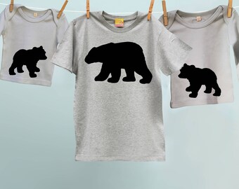 May include: Three gray t-shirts with black bear silhouettes. The largest shirt has a large bear silhouette, the medium shirt has a medium bear silhouette, and the smallest shirt has a small bear silhouette.