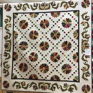 May include: A white quilt with a brown, green and red floral border. The centre of the quilt features a repeating pattern of colourful pinwheels.