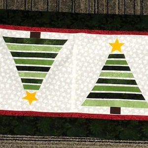May include: A green and black striped Christmas tree table runner with four trees and gold stars. The runner has a red and green border.