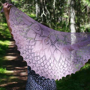 May include: A delicate, lacy shawl in a soft purple hue, draped over a person's shoulders in a forest setting. The shawl features intricate floral patterns and a scalloped edge.