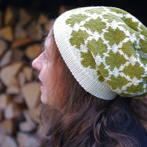 May include: A woman wearing a white and green knitted hat with a geometric pattern. The hat is slouchy and has a wide brim.