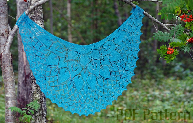 May include: A teal blue crocheted shawl with a lacy pattern hangs from a tree branch. The shawl is made with a delicate stitch and has a scalloped edge.