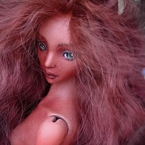 Pode incluir: Uma boneca articulada de pele bronzeada, com longos cabelos ondulados castanho-avermelhados e olhos verde-claros. A boneca apresenta uma articula&ccedil;&atilde;o de ombro vis&iacute;vel e o texto Amado Gravagno Porcelain Ball jointed dolls no canto inferior.