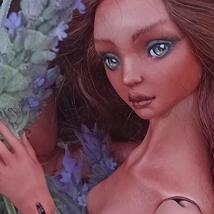 Pode incluir: Uma boneca de porcelana articulada com longos cabelos castanho-avermelhados e olhos azul-claros. A boneca apresenta articula&ccedil;&otilde;es vis&iacute;veis nos ombros e bra&ccedil;os. O texto Amado Gravagno Porcelain Ball jointed dolls est&aacute; presente na imagem.