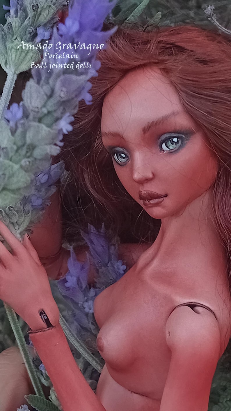 Pode incluir: Uma boneca de porcelana articulada com longos cabelos castanho-avermelhados e olhos azul-claros. A boneca apresenta articula&ccedil;&otilde;es vis&iacute;veis nos ombros e bra&ccedil;os. O texto Amado Gravagno Porcelain Ball jointed dolls est&aacute; presente na imagem.