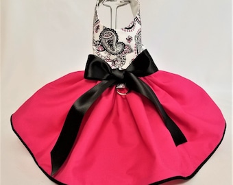May include: A pink dog dress with a white and black paisley print bodice, a black satin bow, and a black trim around the skirt.