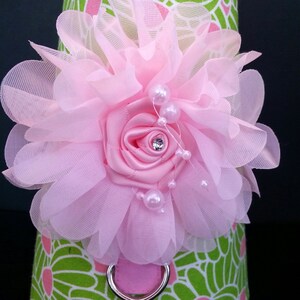 May include: A pink flower with a pearl and rhinestone embellishment, attached to a green and pink patterned fabric.
