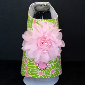 May include: A green and pink floral dog harness with a pink flower accent. The harness has a metal ring for attaching a leash.