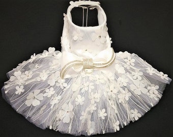 May include: White tulle dog dress with a large white satin bow and a rhinestone embellishment. The dress is decorated with white flower appliques.