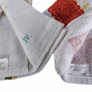 Puede incluir: Dos toallas de cocina blancas con estampados florales coloridos. Las toallas est&aacute;n dobladas por la mitad y muestran las instrucciones de cuidado en la etiqueta. La etiqueta dice 100% algod&oacute;n, lavar a m&aacute;quina con agua fr&iacute;a, secar en secadora a baja temperatura, ciclo delicado, no usar blanqueador, no planchar, hecho en China.