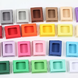 Könnte beinhalten: Ein Set mit 36 kleinen Pappkartons mit einem Fenster vorne. Die Kartons sind in verschiedenen Farben, darunter Schwarz, Grau, Rot, Orange, Gelb, Grün, Blau, Lila und Weiß.