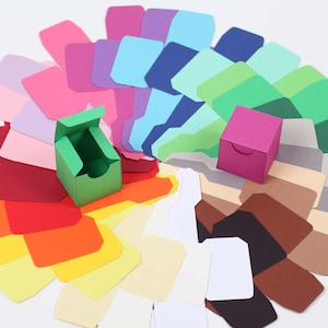 Könnte beinhalten: Eine Auswahl an Kartonpapier in Fächerform, mit zwei kleinen grünen und rosa Geschenkboxen in der Mitte.