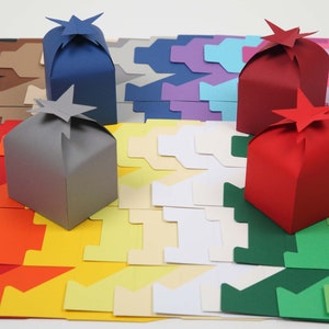 Könnte beinhalten: Sortiment an bunten Papiergeschenkkartons mit sternförmigen Oberseiten. Die Kartons sind in Reihen auf einer weißen Oberfläche angeordnet. Die Kartons sind in verschiedenen Farben erhältlich, darunter Rot, Blau, Grün, Gelb und Grau.