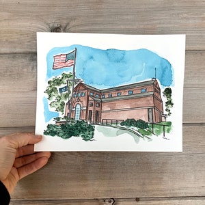May include: Watercolor painting of a brick building with a flagpole and an American flag. The building has a brown roof and windows. There are trees and bushes in the foreground.
