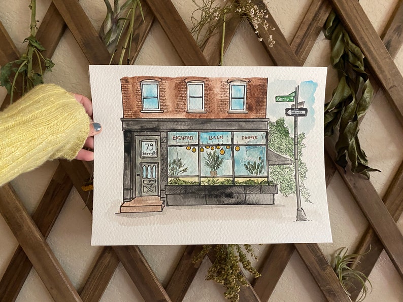 May include: Watercolor painting of a storefront with a black awning and a sign that says "79 Kenny St." The storefront has large windows with the words "Breakfast", "Lunch", and "Dinner" written on them. There are yellow lights hanging from the ceiling inside the storefront. The building is brick with three windows on the top floor.