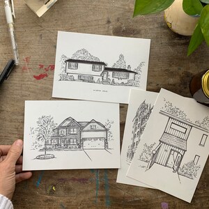 K&ouml;nnte beinhalten: Drei Schwarzwei&szlig;-Tintenzeichnungen von H&auml;usern auf wei&szlig;em Karton. Die Zeichnungen zeigen verschiedene Hausstile, darunter ein Ranchhaus, ein zweist&ouml;ckiges Haus und ein kleines H&auml;uschen.