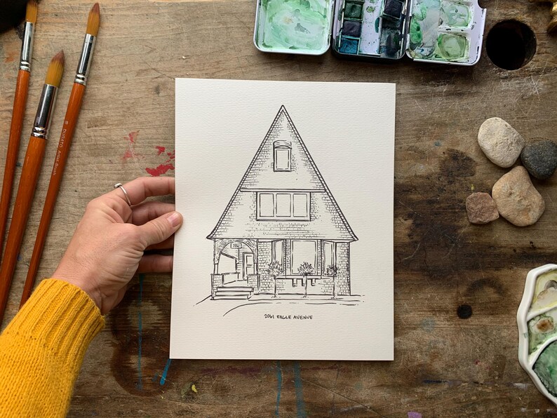 May include: A black and white line drawing of a house with a triangular roof. The house has a porch with a door and windows. The drawing is on a white background and says "304 Cedar Avenue" at the bottom.