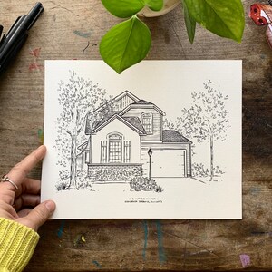 K&ouml;nnte beinhalten: Schwarz-wei&szlig;-Zeichnung eines Hauses mit Garage, B&auml;umen und einer Stra&szlig;enlaterne. Das Haus hat eine Backsteinfassade und ein Satteldach. Die Zeichnung ist auf wei&szlig;em Hintergrund.