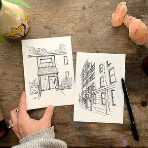 May include: Two black and white line drawings of buildings. The first drawing is of a small building with a door and windows. The second drawing is of a larger building with multiple windows.