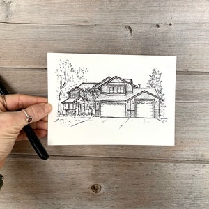 K&ouml;nnte beinhalten: Schwarz-wei&szlig;-Zeichnung eines Hauses mit einer Doppelgarage. Das Haus hat einen gro&szlig;en Vorgarten mit B&auml;umen und B&uuml;schen.