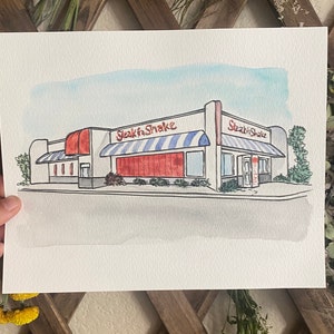 Custom artwork shows an image of a restaurant on 8x10” watercolor paper. The watercolor painting sits in the middle of the paper, with a 2-3 inch white border that allows for nice matting and framing.