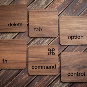 May include: Six wooden coasters with different computer keyboard keys engraved on them. The keys are: delete, tab, option, fn, command, and control.