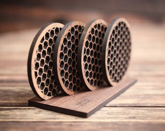May include: Set of four wooden coasters with a honeycomb design. The coasters are arranged in a stack and are sitting on a wooden base.
