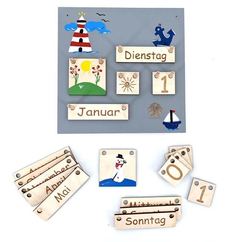 May include: Wooden calendar with colorful painted images and wooden pieces for days, months, and days of the week. The calendar includes images of a lighthouse, a sun, a flower, a snowman, and a sailboat. The calendar also includes the words "Januar", "Dienstag", "Sonntag", "Mittwoch", "Mai", "April", "November", "Okt", and "Juli".
