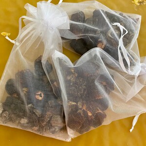 May include: Two white mesh bags filled with dried black mushrooms. The bags are tied with white ribbons.