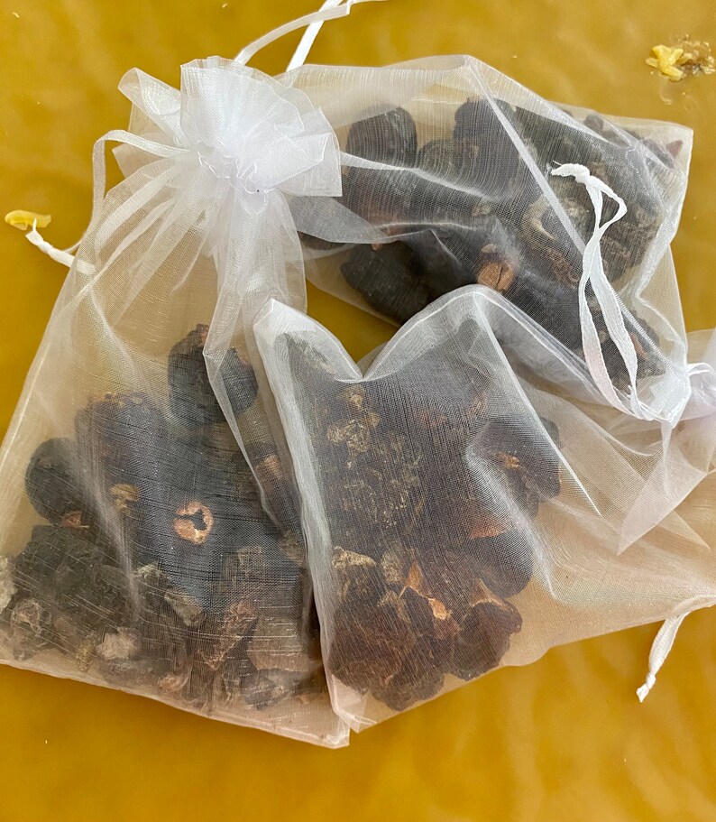 May include: Two white mesh bags filled with dried black mushrooms. The bags are tied with white ribbons.