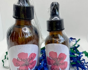 May include: Two amber glass bottles of body oil with black droppers, wrapped in clear plastic. Each bottle has a white label with the text "Eternal Summer Body Oil" and a pink flower design. The bottles are surrounded by blue and green paper shreds.