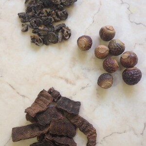 May include: A collection of dried herbs and nuts, including brown and black dried leaves, and brown round nuts.