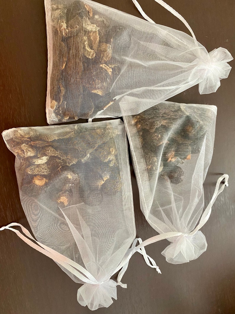 May include: Three white mesh bags filled with dried black mushrooms. The bags have white drawstrings and are tied at the top.