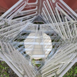 May include: A clear acrylic geometric shelf unit with multiple levels and a grid pattern. The shelf unit is empty and appears to be made of several stacked pieces.