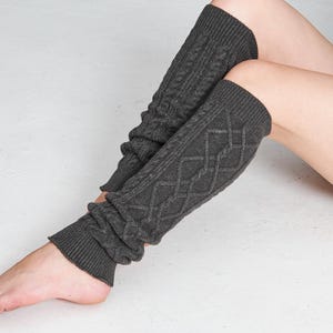 May include: Charcoal grey cable knit leg warmers. These leg warmers feature a ribbed cuff and a diamond pattern on the leg. The leg warmers are made of a soft, warm material, perfect for cold weather. They are designed to be worn over the calf.
