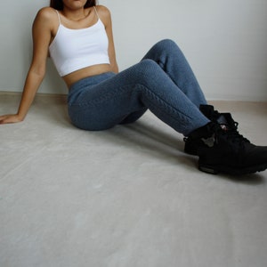 Woman sitting casually on the floor in denim blue cable knit pants paired with a white crop top and black boots.