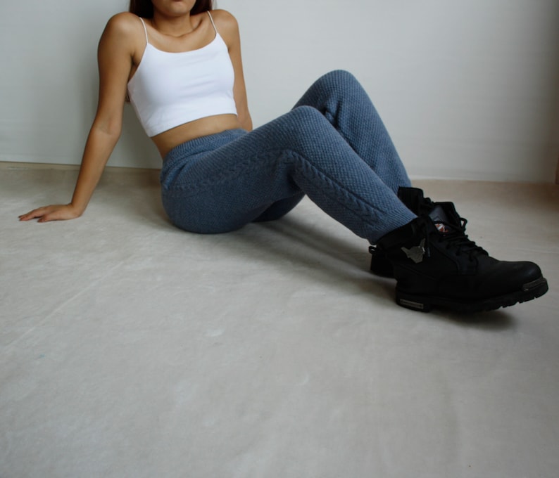 Woman sitting casually on the floor in denim blue cable knit pants paired with a white crop top and black boots.