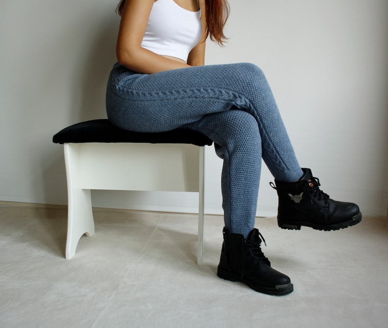 Woman seated on a white bench wearing denim blue cable leggings, showing the textured knit pattern from hip to ankle.