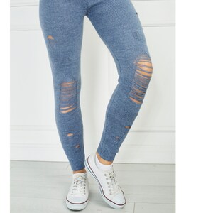 Puede incluir: Leggings de punto azul con un dise&ntilde;o desgastado y rasgado con m&uacute;ltiples aberturas horizontales a lo largo de las piernas, combinados con zapatillas de lona blancas que tienen un borde rojo y azul en las suelas de goma y cordones blancos.
