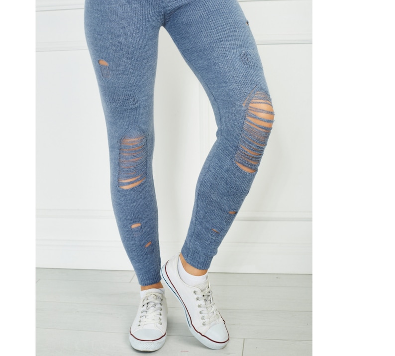 Puede incluir: Leggings de punto azul con un dise&ntilde;o desgastado y rasgado con m&uacute;ltiples aberturas horizontales a lo largo de las piernas, combinados con zapatillas de lona blancas que tienen un borde rojo y azul en las suelas de goma y cordones blancos.