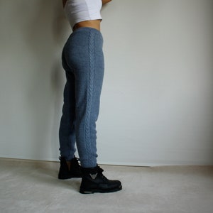 Side profile of denim blue knitted leggings styled with black ankle boots, highlighting the long cable knit detail along the outer leg.