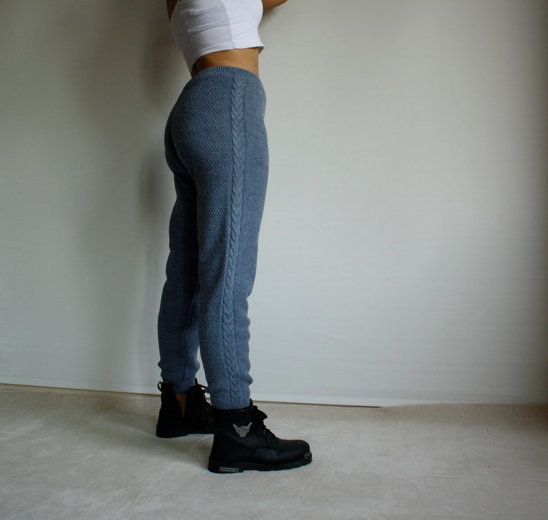 Side profile of denim blue knitted leggings styled with black ankle boots, highlighting the long cable knit detail along the outer leg.